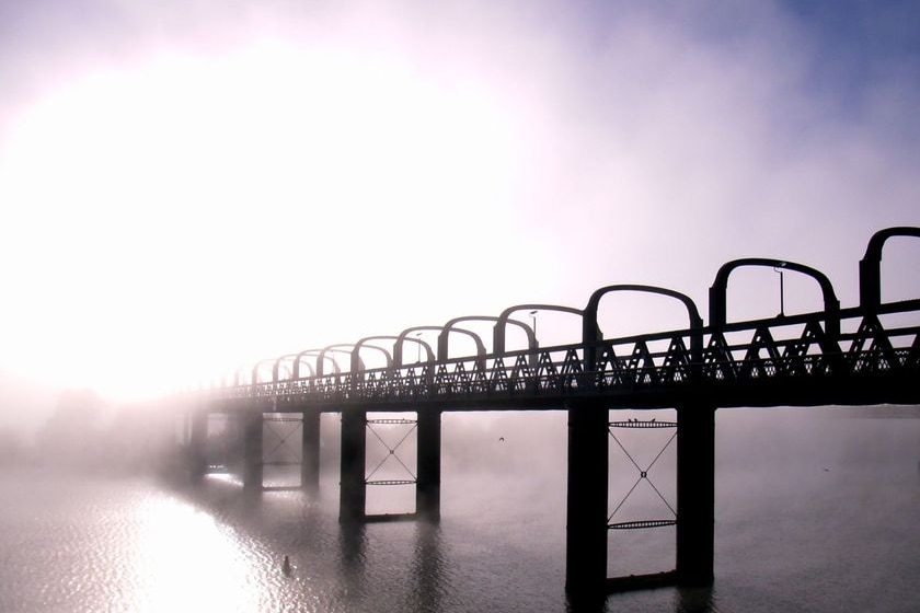A bridge over a river disappears into the morning fog