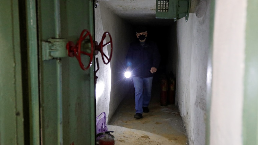 A man holding a flashlight walks down a tunnel.
