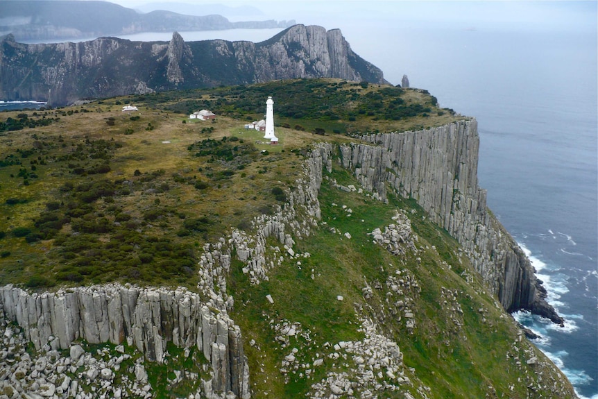 A wide shot of a lighthouse on an island with rocky cliff edges