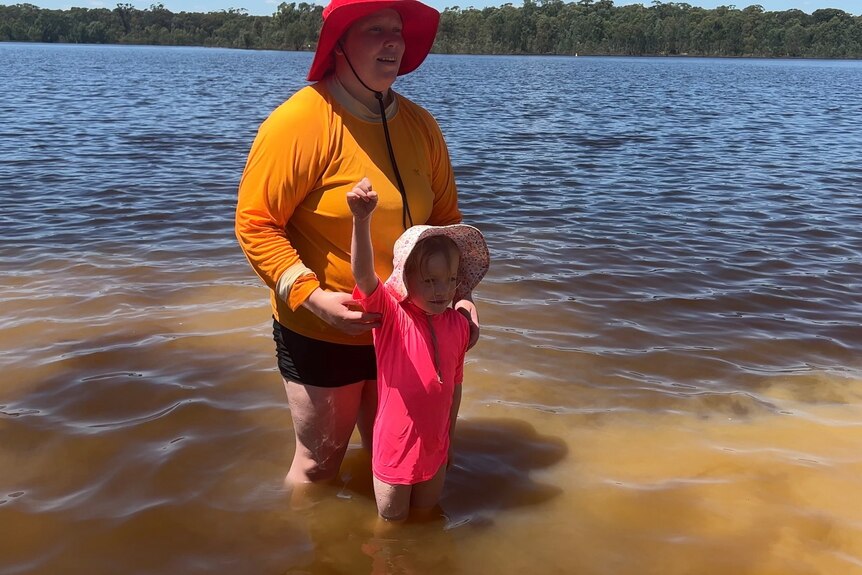 little girl standing with one arm up, in front of a life saver, in shallow water 