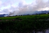 A screenshot from a video shows a plume of smoke and mountains in the distance.