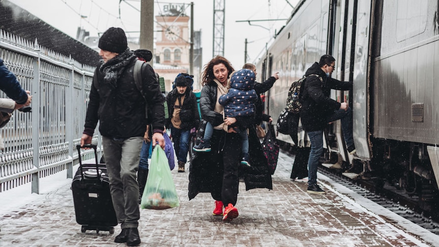 A woman walks along a platform at the Kyiv train station carrying a small child, March 1, 2022. She looks worried.