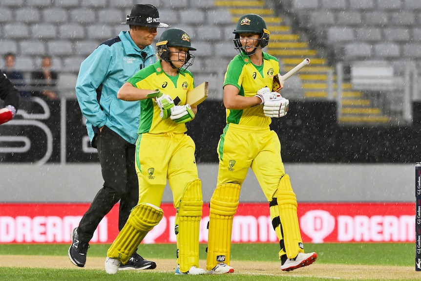 Two female cricket player walking off the pitch after a game was delayed due to the rain.