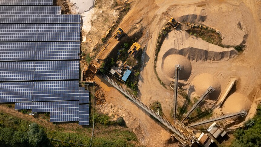 An aerial view looking down at a solar panel farm next to a sand mine with a dozer operating