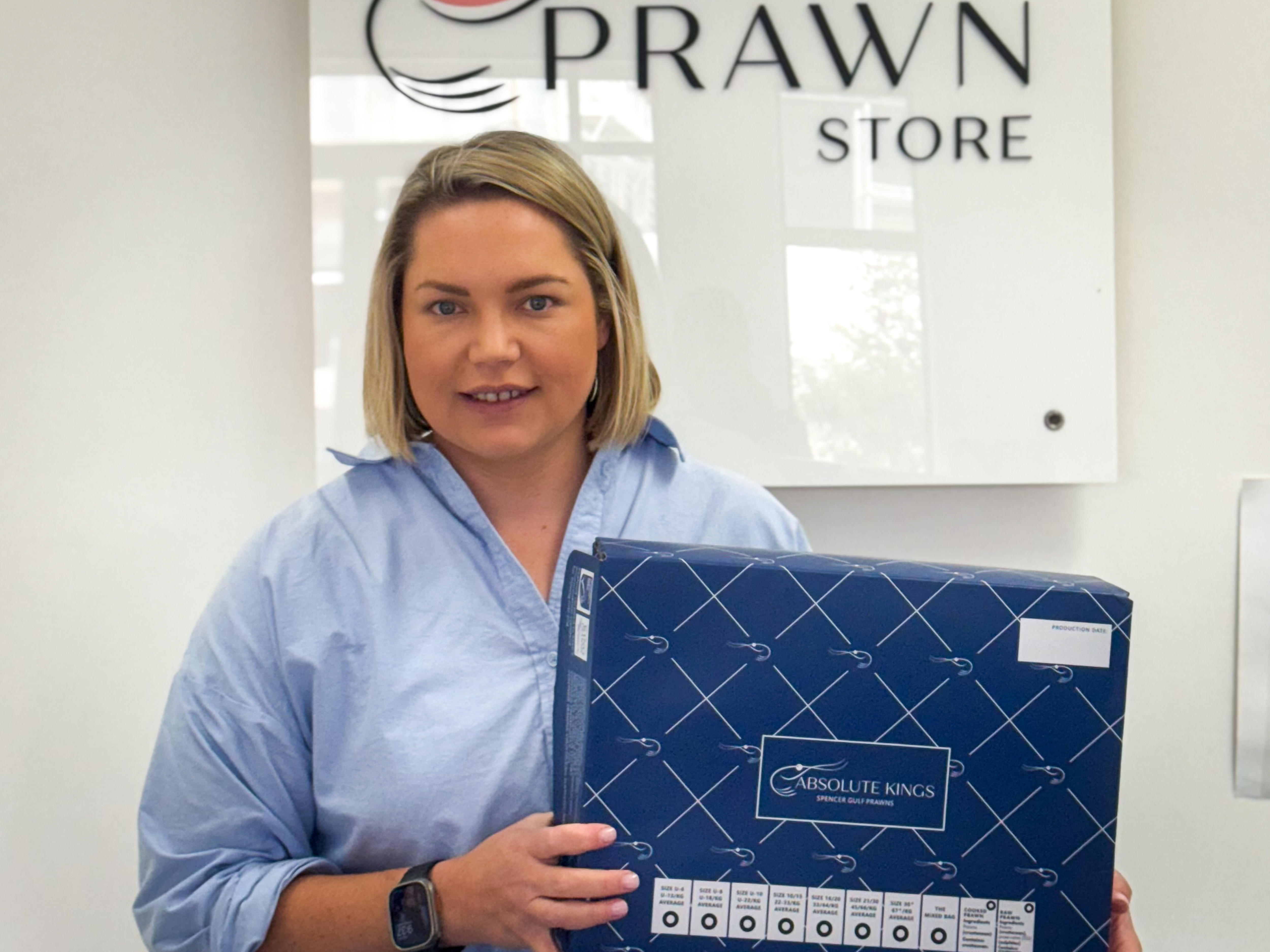 Uma mulher segura uma caixa de frutos do mar e sorri.