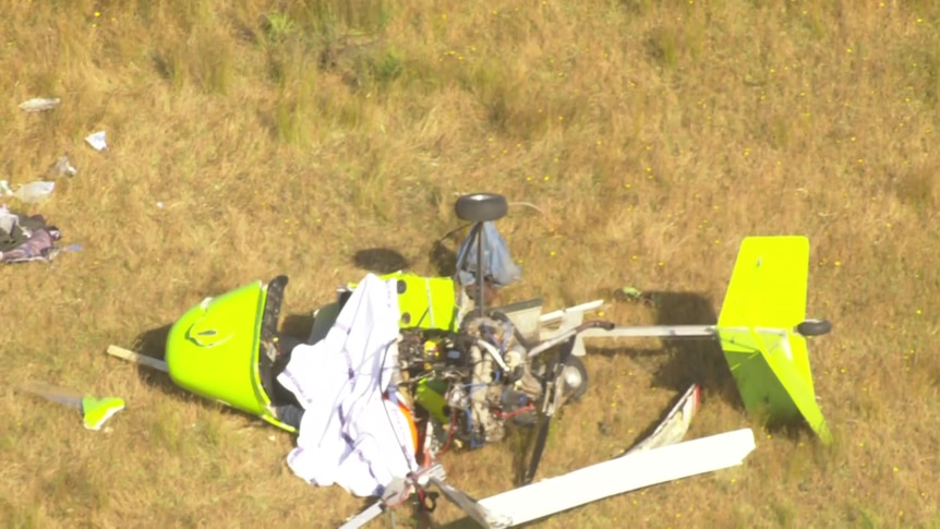 An aerial view of the wreckage of a small, green aircraft on grass.