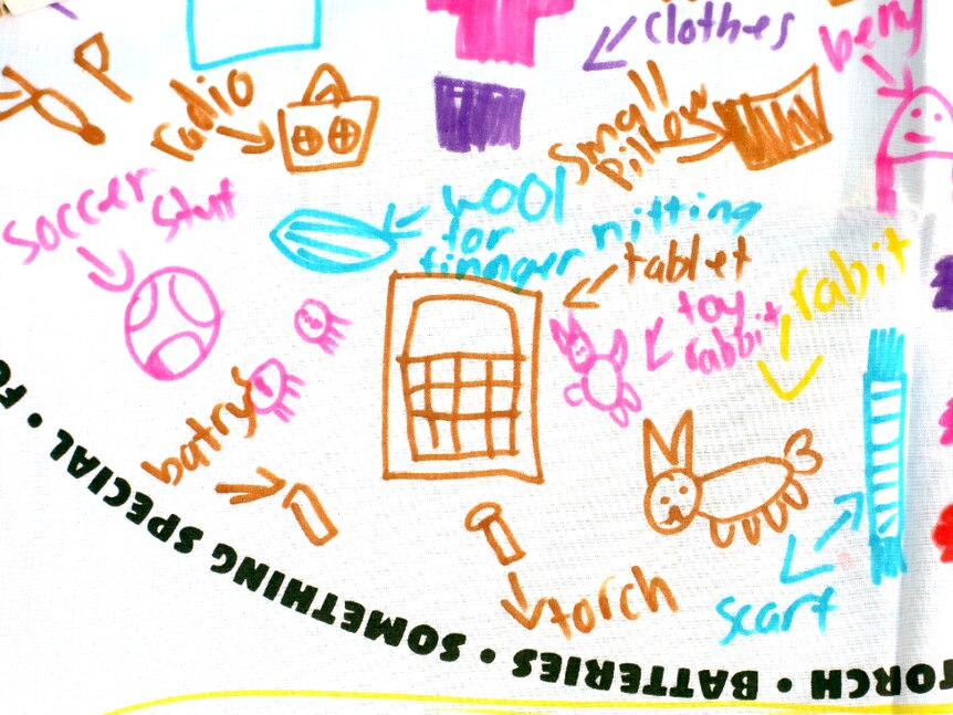 A white pillowcase with child's drawing and writing of items to include in an emergency including, small pillow, radio, clothes.