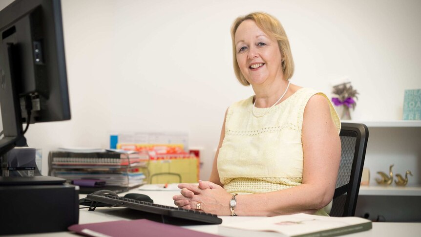 Dr Kathleen Baird sits smiling at a desk.