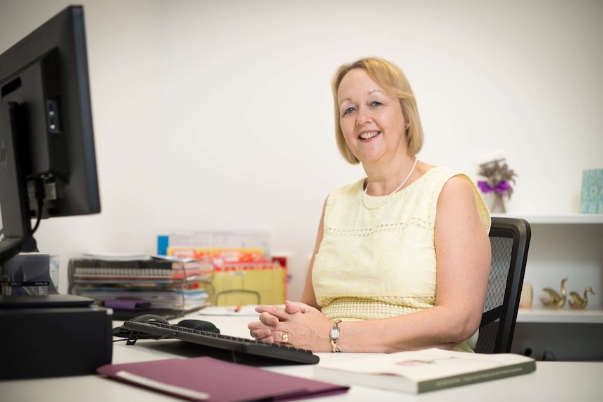 Dr Kathleen Baird sits smiling at a desk.
