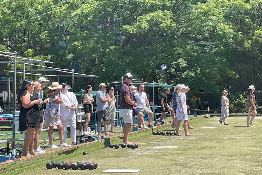 Men and women play outdoor lawn bowls on a green lawn