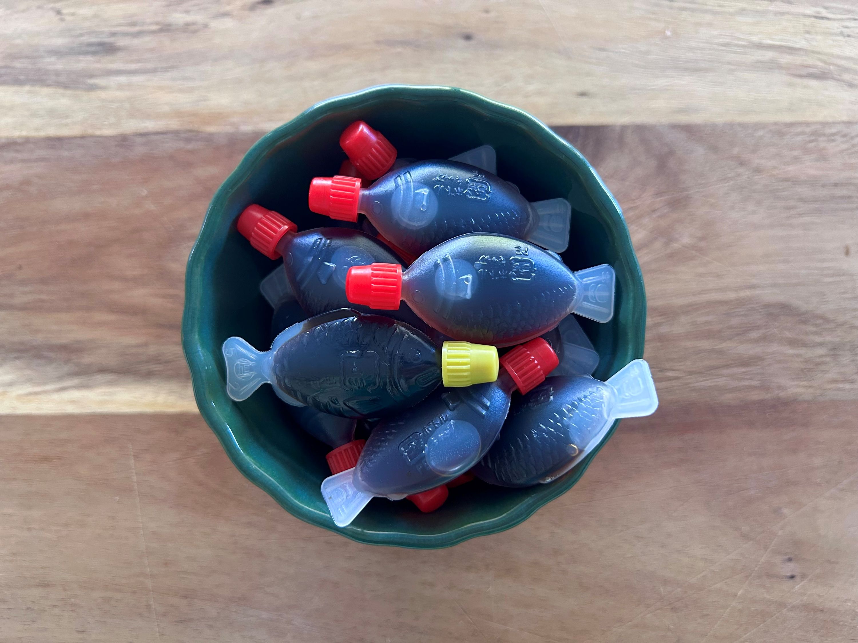 A green bowl of small plastic fish filled with soy sauce, on a wooden surface.