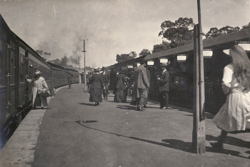 A black and white image of people standing adjacent two trains on a platform.