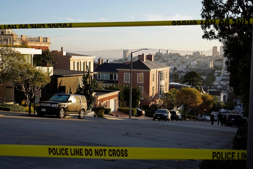 Police tape blocks a street with a large house in the centre of the frame of a residential street.
