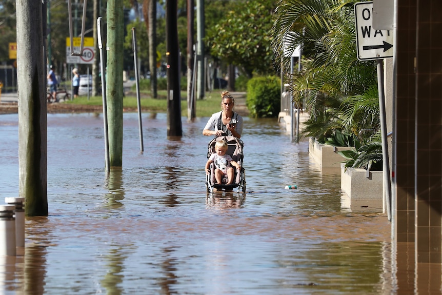 A woman with a pram walking through flood waters.