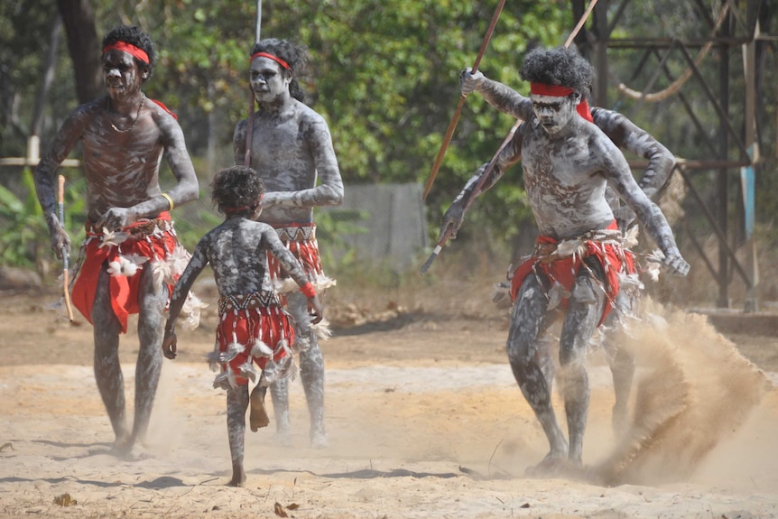 Men in traditional Indigenous paint and clothing dance.