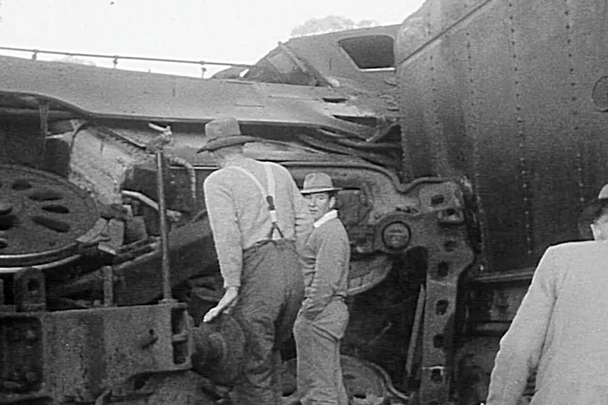 A black and white image of two people standing closely to the tipped train inspecting it