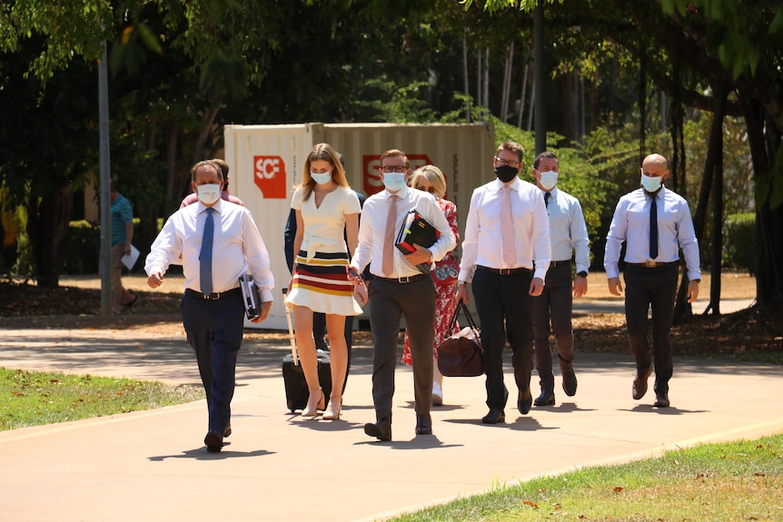 A group of people arrive at court. They are wearing masks.