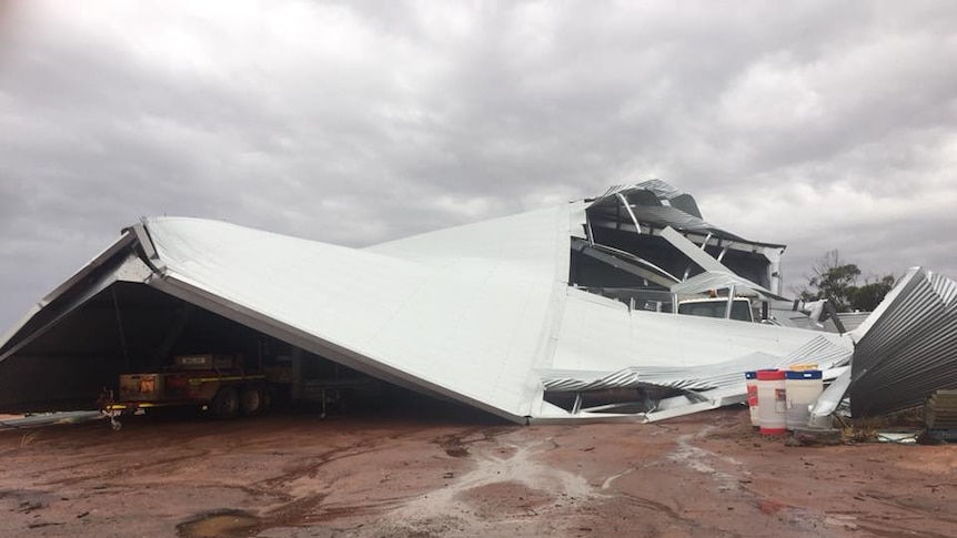 A large shed lies almost completely collapsed with a truck underneath it.