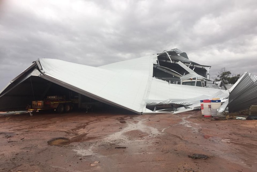 A large shed lies almost completely collapsed with a truck underneath it.