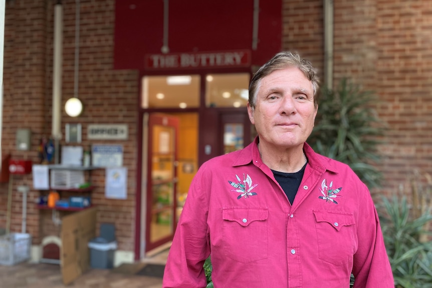 A man in a red groovy shirt stands in front of the Buttery office 