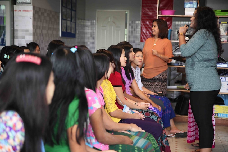 Woman speaks to a group of seated women through a microphone