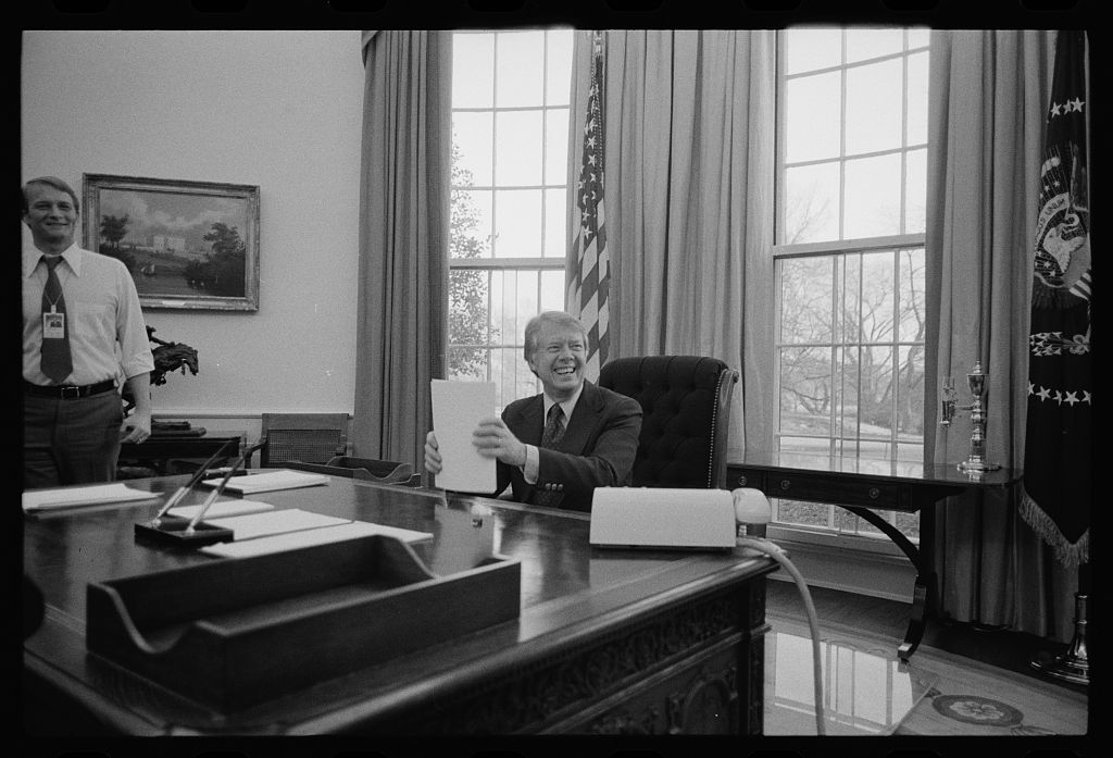 Jimmy Carter laughs to someone out of shot in the Oval Office.