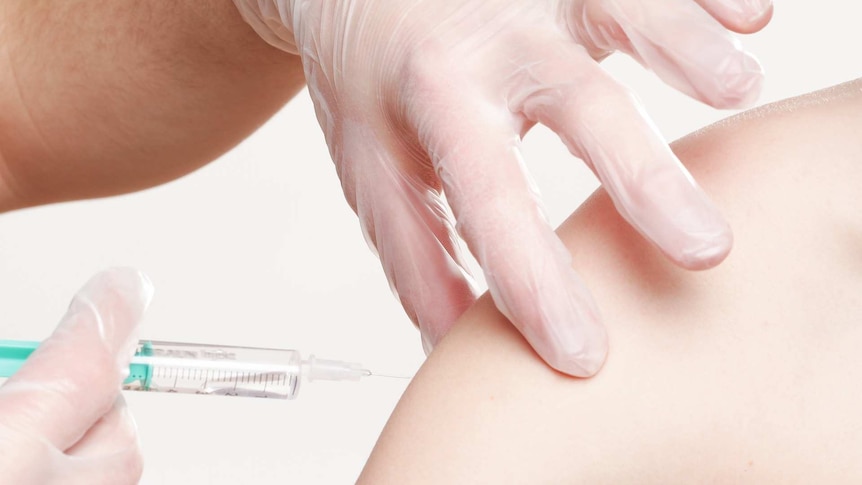 A needle containing a vaccine is administered to a human arm.