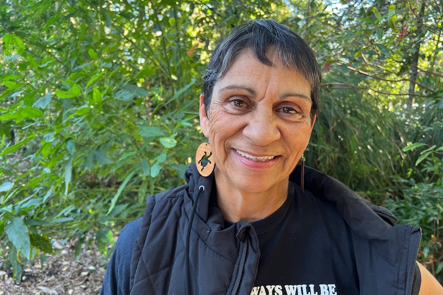 A portrait of Monica Morgan smiling, standing in a leafy area.