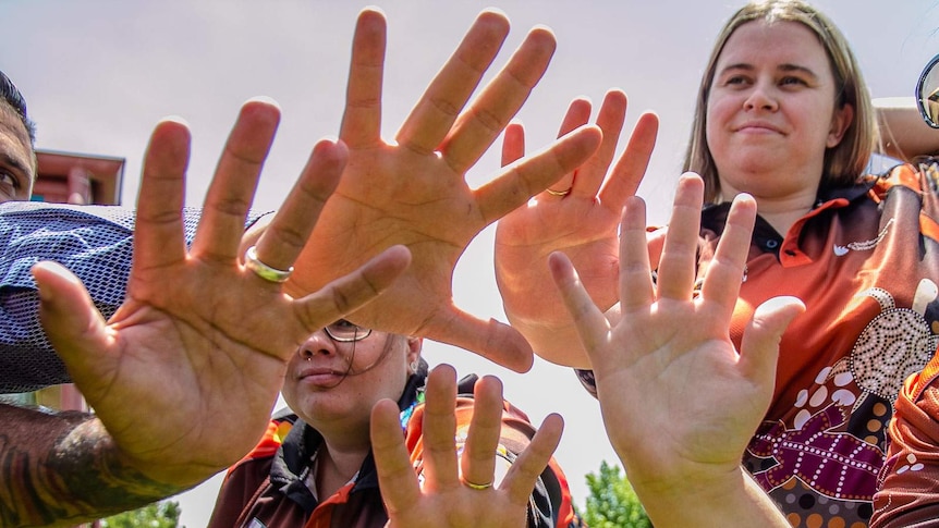 Five male and female hands held palms out with light shining through in the background