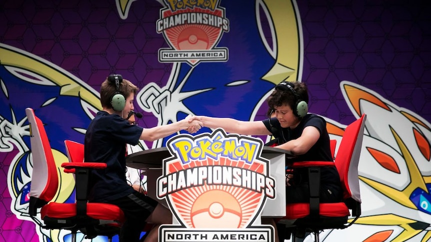 Two boys with headphones on shake hands at a gaming championship.