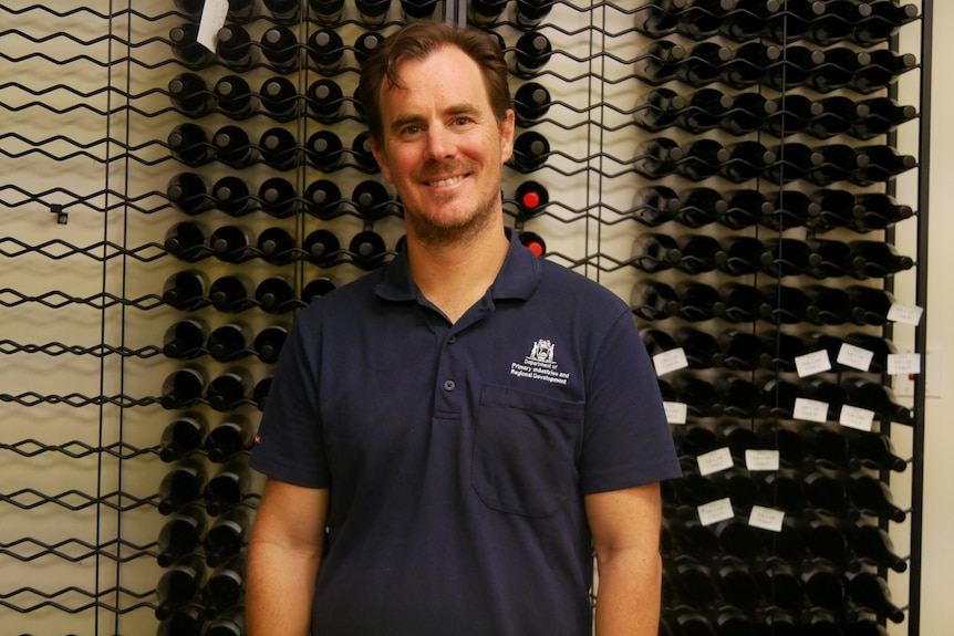 A man stands in front of a wine rack.