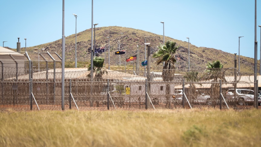 Image of prison buildings behind a high razor-wire security fence