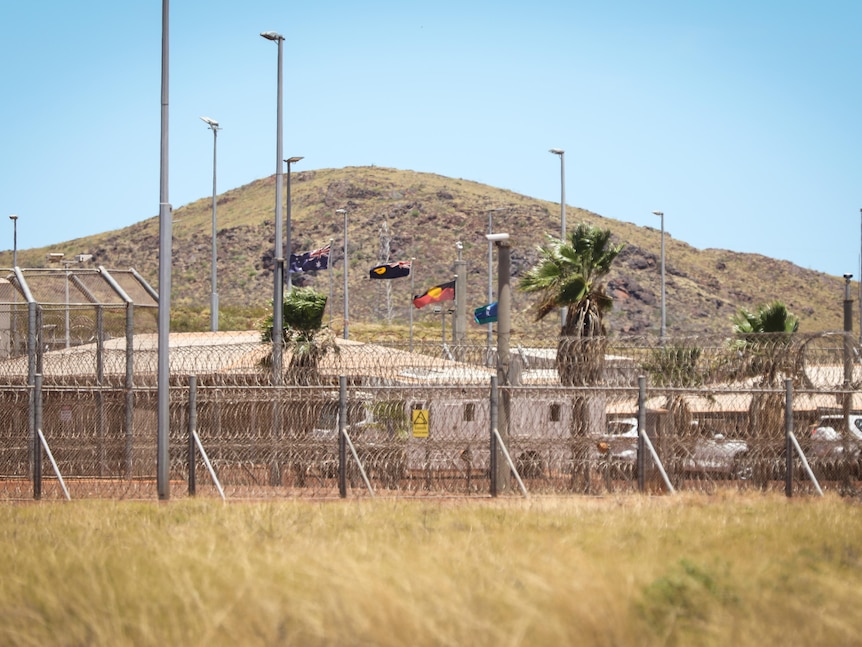 Image of prison buildings behind a high razor-wire security fence