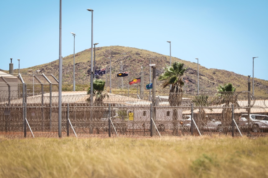 Image of prison buildings behind a high razor-wire security fence