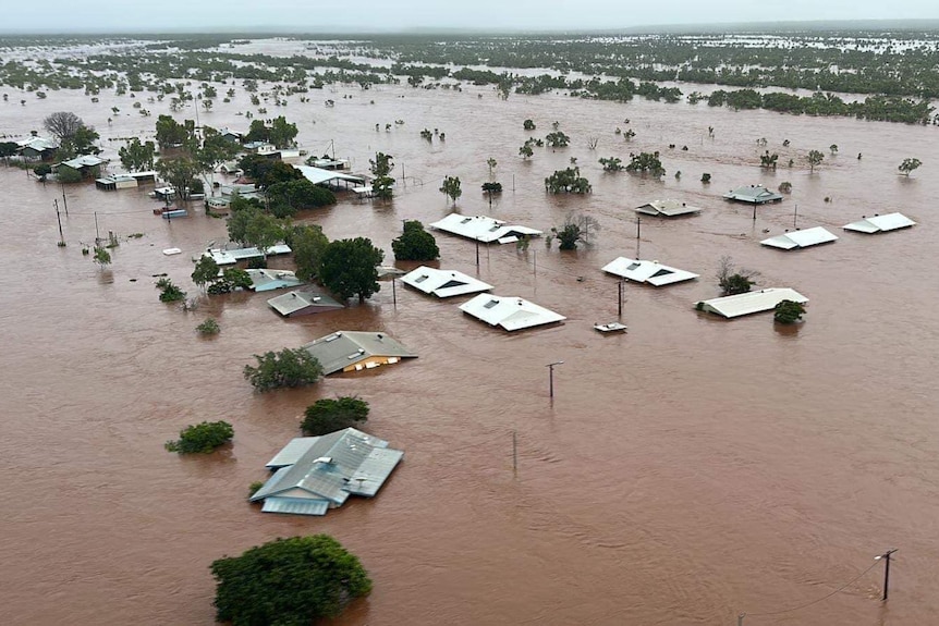 An aerial view of flooding in a remote community, showing water up to the rooftops of houses.