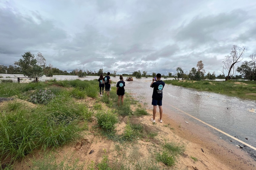 A group of people stand near a flooded road