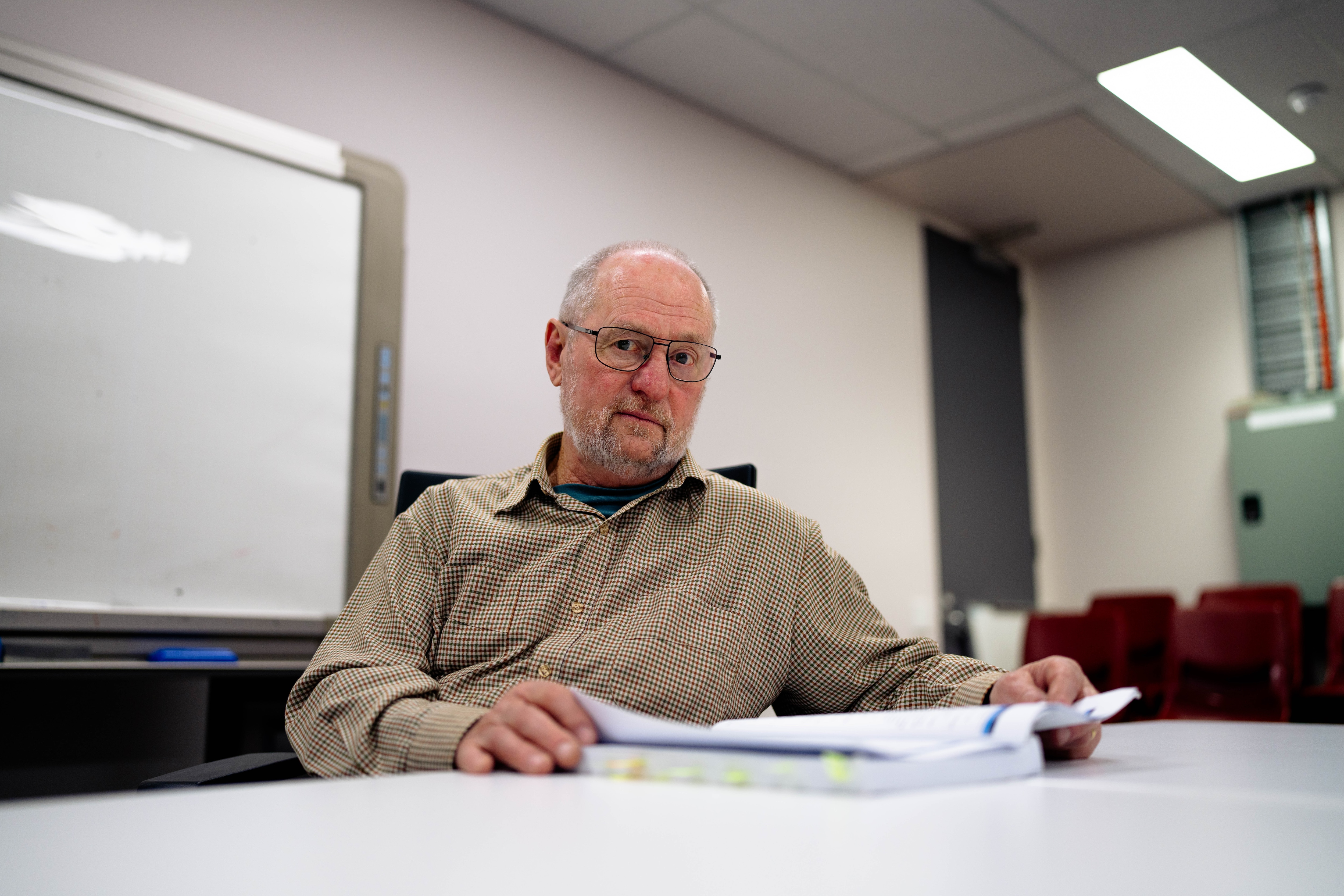 Mid shot of Patrick, looking straight into the camera, at a large table looking at a report document with sticky notes.
