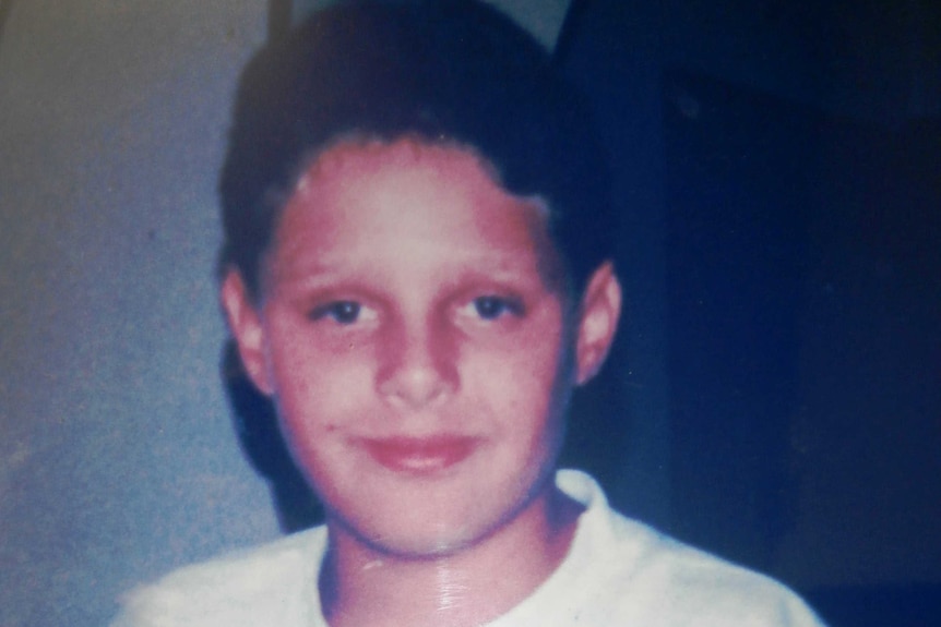 A photograph of a teenage boy wearing a white t-shirt.