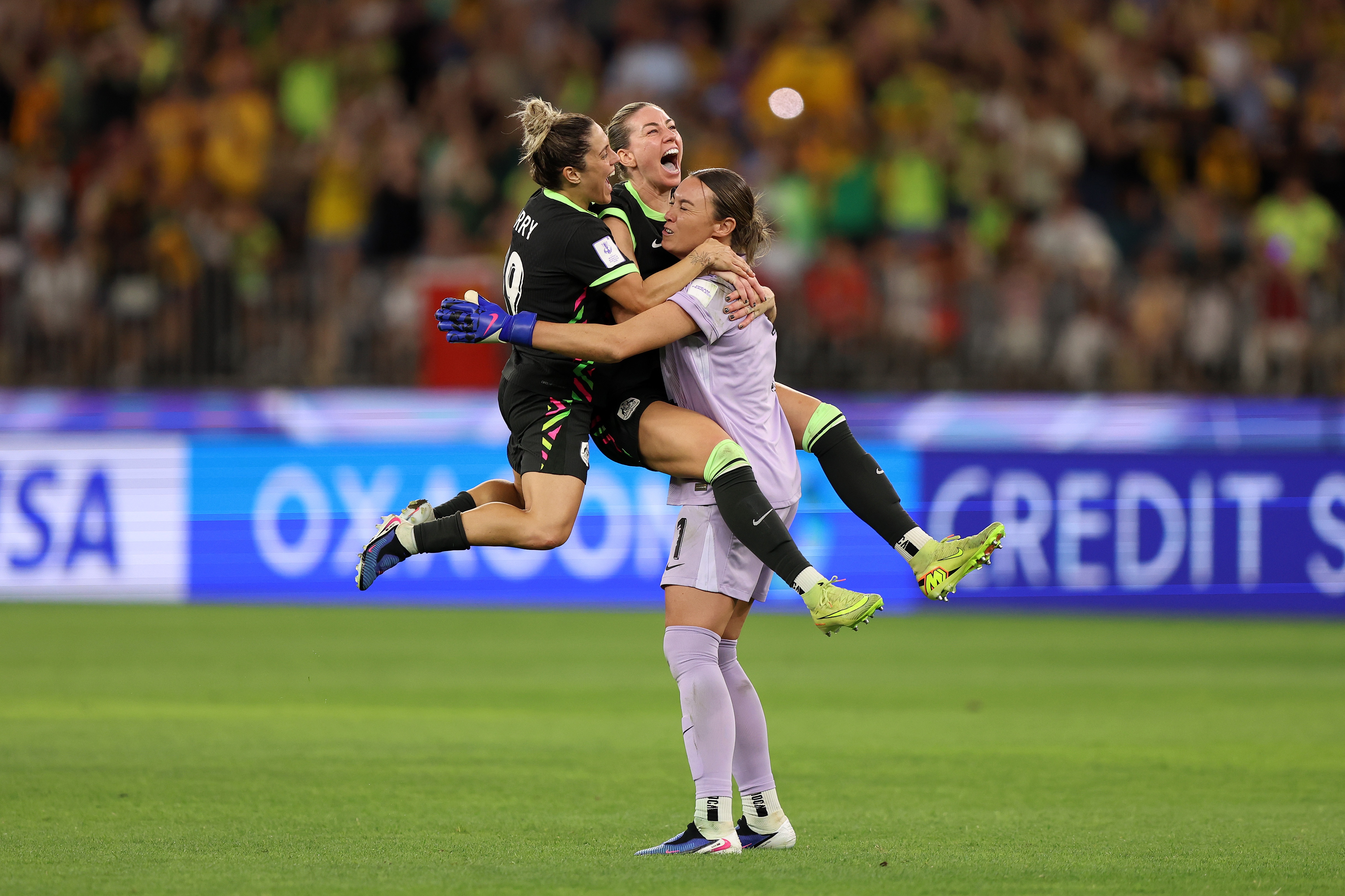 Three Matildas players jump on each other and celebrate