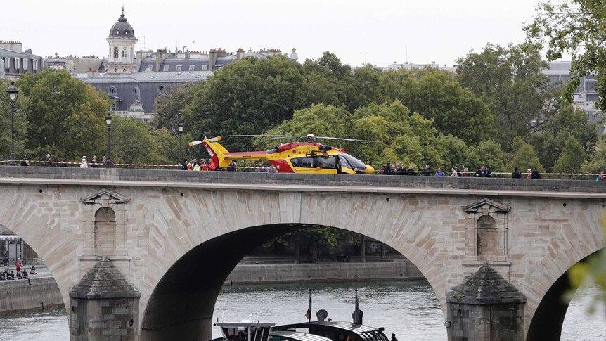 A red and yellow helicopter sits on an historic-looking bridge, which has red and white police tape blocking off one side.