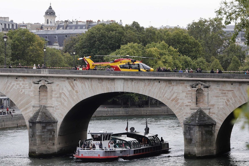 A red and yellow helicopter sits on an historic-looking bridge, which has red and white police tape blocking off one side.