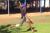 Aboriginal boy kicking football.