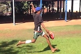 Aboriginal boy kicking football.