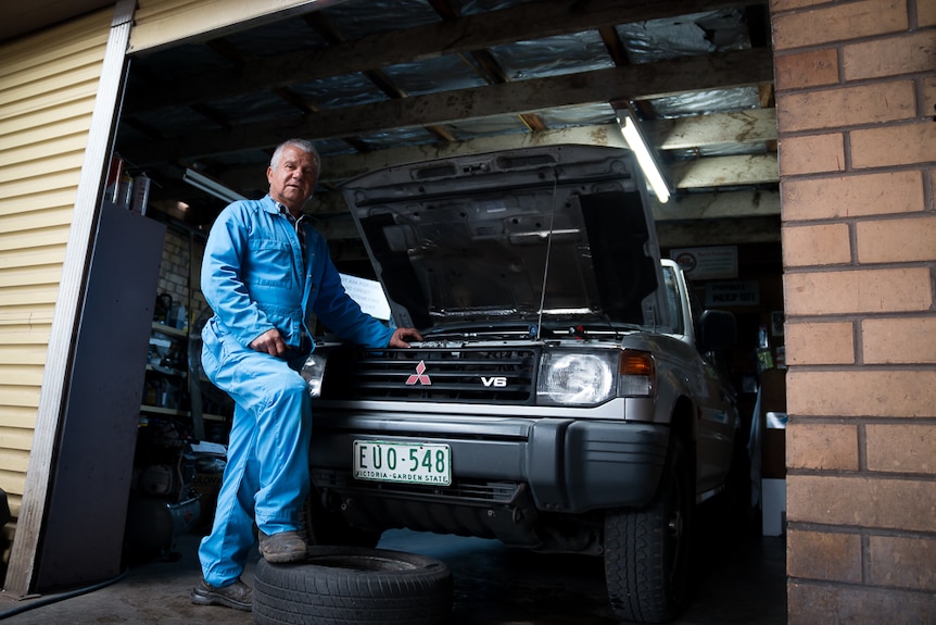 Ylmiz Hassan stands at the entrance to his garage leaning against a car he is repairing.