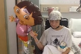 William Lo in a hospital bed holding a balloon.