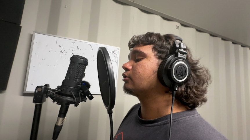 A young Indigenous man sings into a microphone.