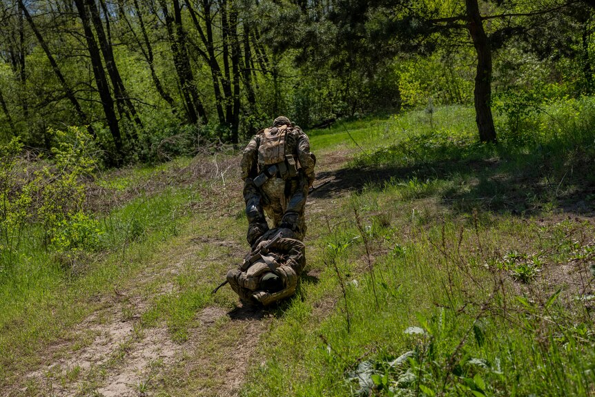 A Ukrainian Border Guard soldier drags another soldier through a forest during training