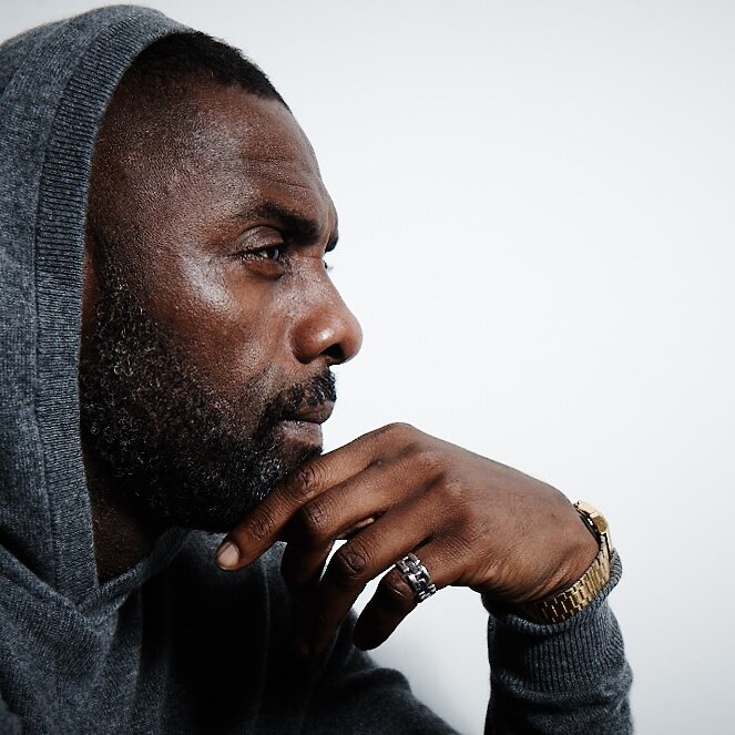 a studio image of idris elba looking sideways with his chin resting on his hand