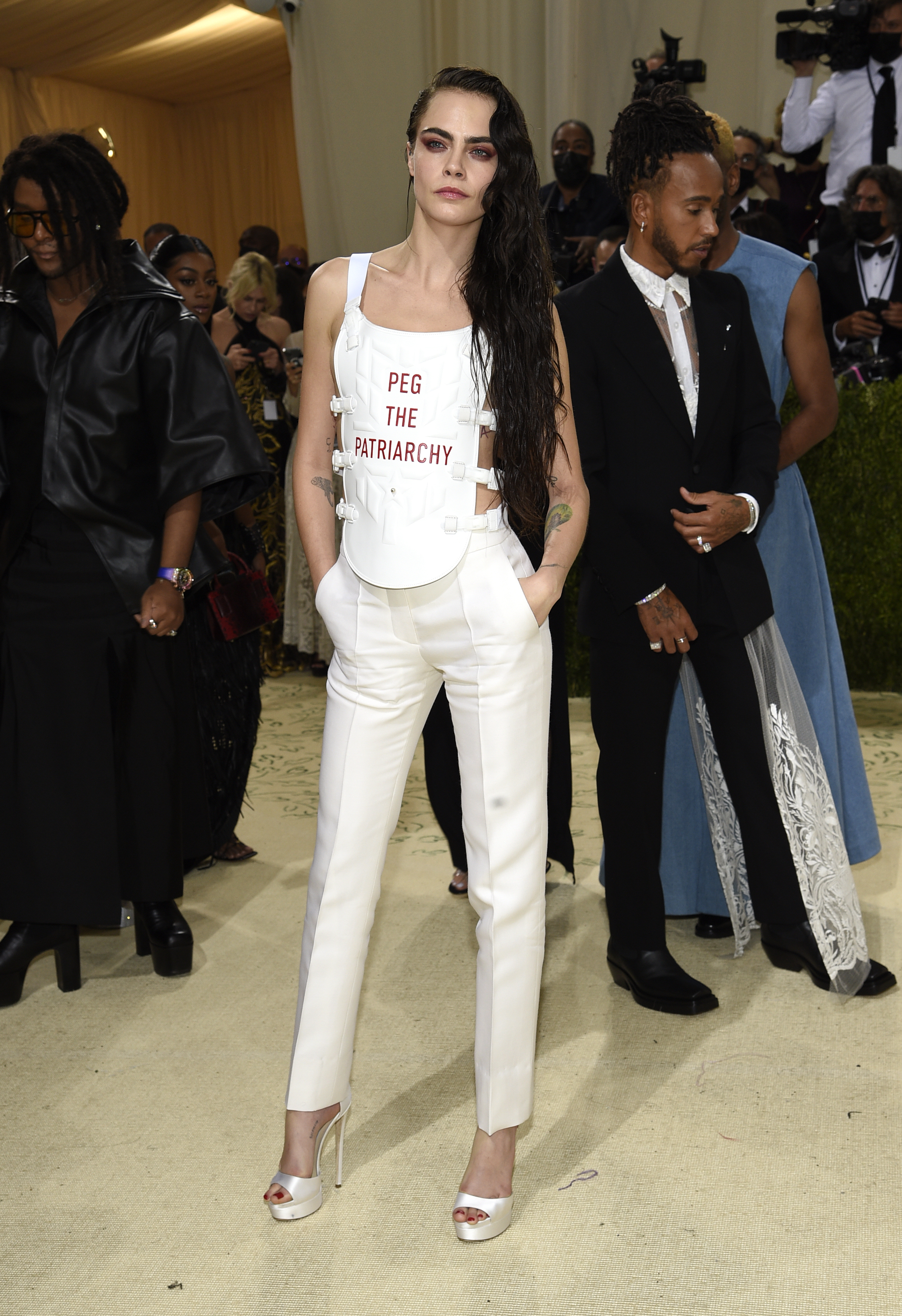 Cara Delevingne wears a white jumpsuit that says "peg the patriarchy" in red letters.