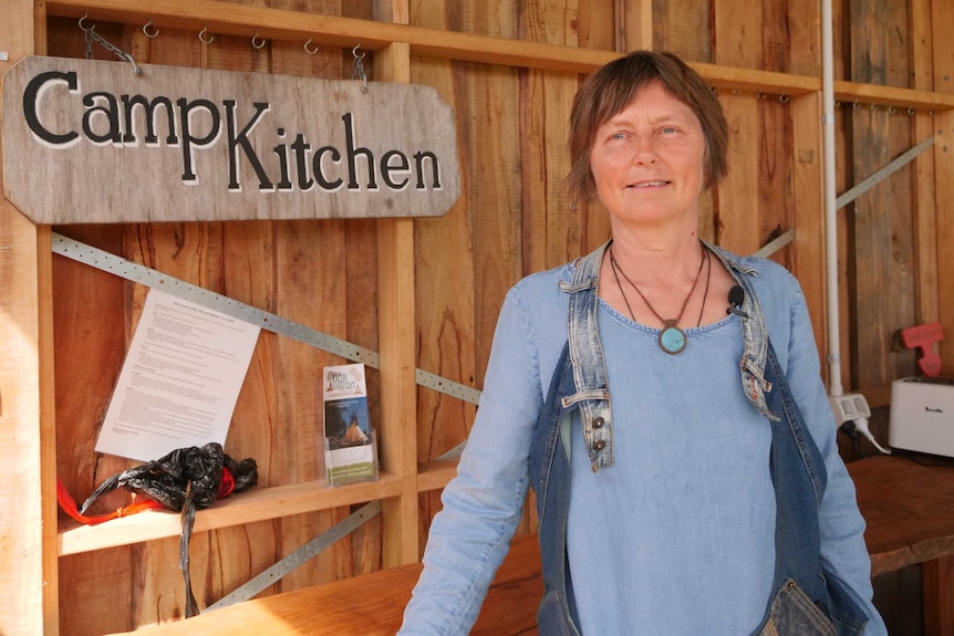 A woman standing in an outside kitchen area leaning on a wooden bench